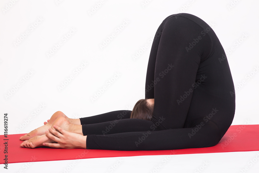 Beautiful athletic girl in black suit doing yoga. karnapidasana asana - knees to ears pose. Isolated on white background.