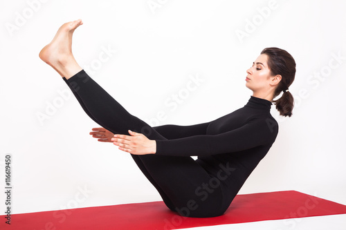 Beautiful athletic girl in black suit doing yoga. naukasana asana - boat pose. Isolated on white background. photo