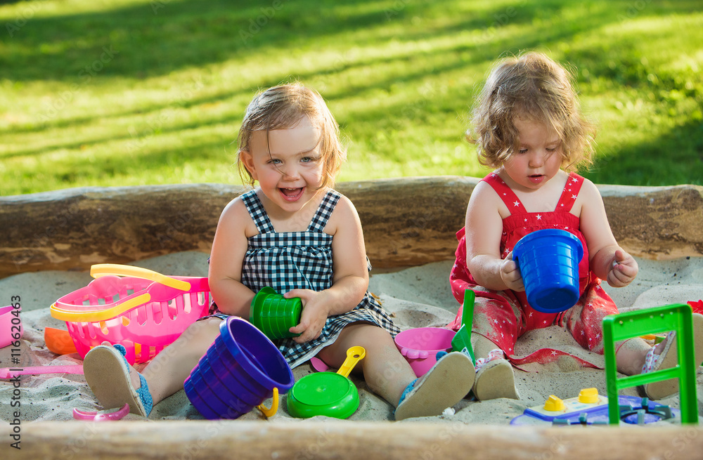 The two little baby girls playing toys in sand The two little baby girls playing toys in sand