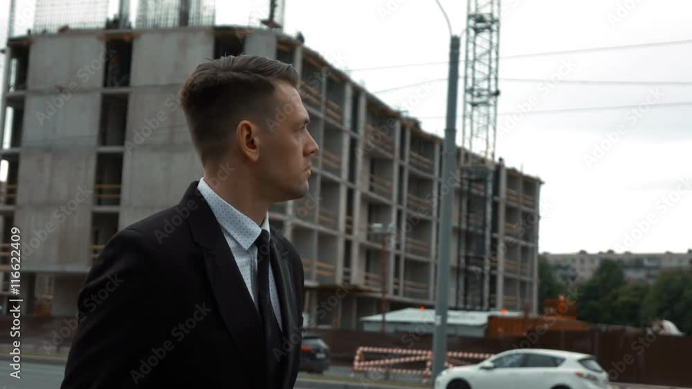 custom made wallpaper toronto digitalSlow motion. Young serious successful businessman in suit and tie walking near the newly constructed building and looking to unfinished construction project at the background. Middle shot.