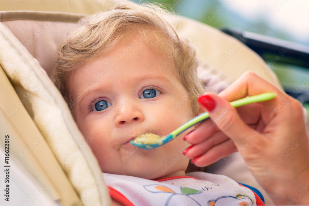 A mother feeding her baby boy with spoon outdoor. A mother feeding her baby boy with spoon outdoor.