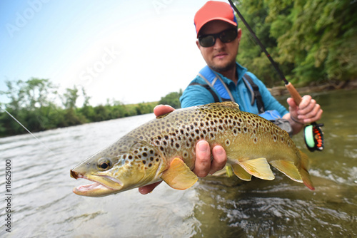 Fototapeta Naklejka Na Ścianę i Meble -  Fly-fisherman holding brown trout out of the water