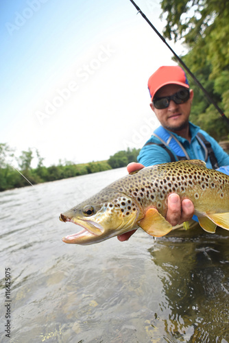 Fototapeta Naklejka Na Ścianę i Meble -  Fly-fisherman holding brown trout out of the water