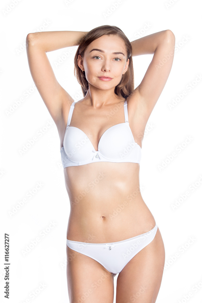 Portrait of beautiful attractive Caucasian young woman wearing white set of  lingerie. Self-confident girl in white bra and panties standing against  white background and looking at camera. Studio shot Stock Photo