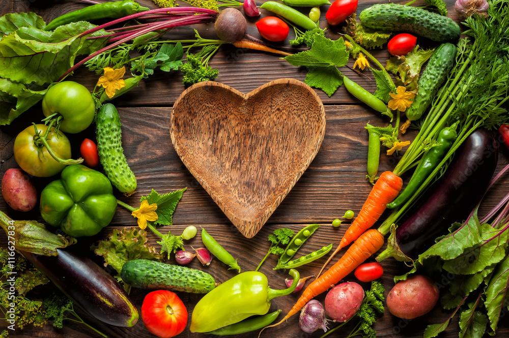 Plate heart shape surrounded with Fresh organic Vegetables on Wooden Background. Healthy Vegetarian food, View from above.