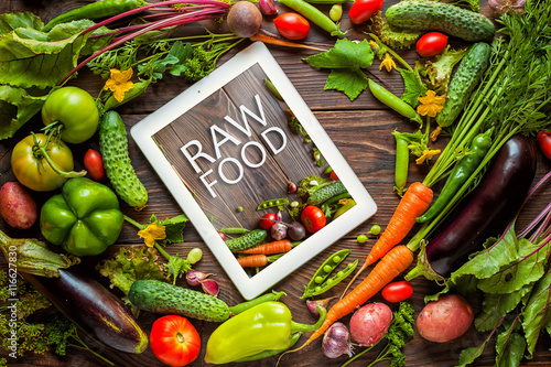 Tablet with text "Raw food" surrounded with Fresh organic Vegetables on Wooden Background. Healthy Vegetarian food, View from above.