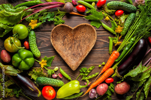 Obraz na płótnie Plate heart shape surrounded with Fresh organic Vegetables on Wooden Background. Healthy Vegetarian food, View from above. w salonie