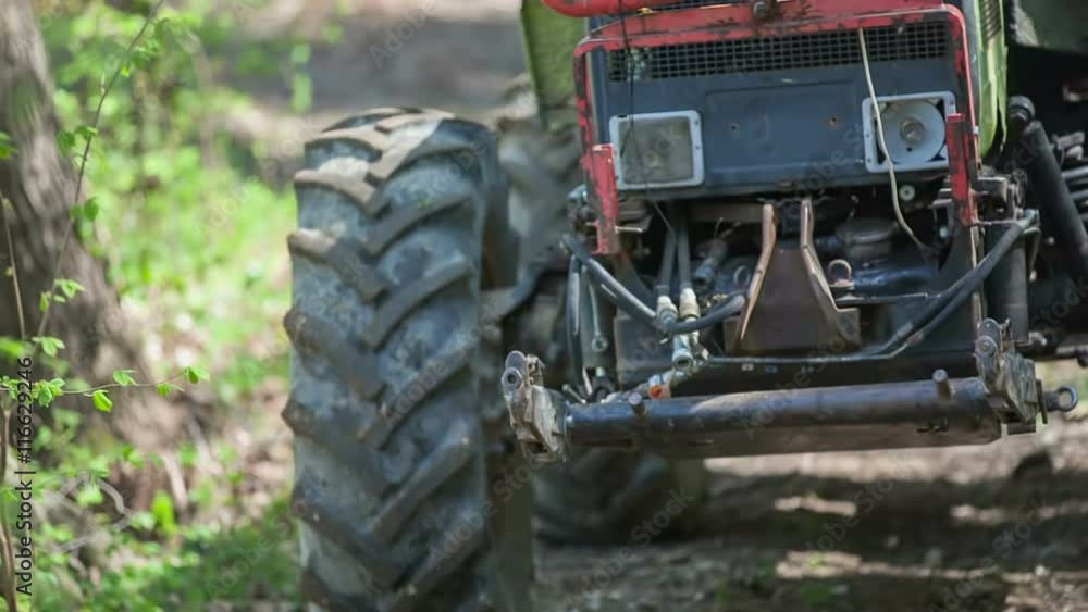 A green tractor is driving backwards on a forest path and it is going to pick up a few tree trunks and then drag them out of a forest. Close-up shot.
A green tractor is driving backwards on a forest path and it is going to pick up a few tree trunks and then drag them out of a forest. Close-up shot.
