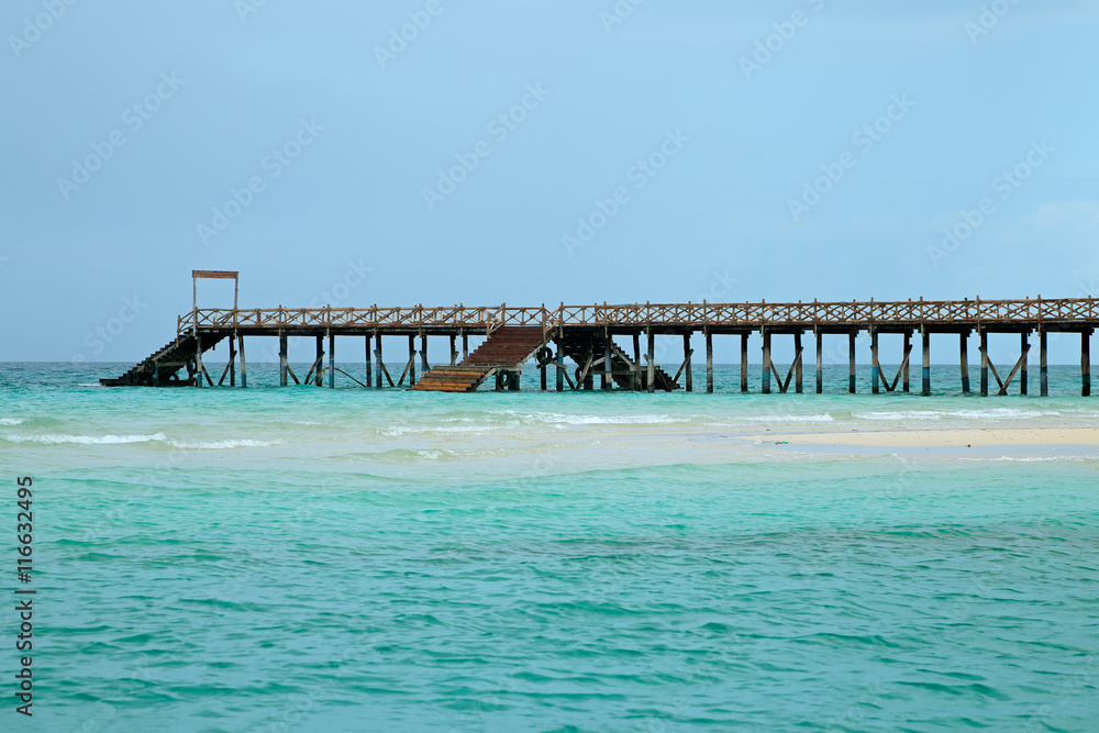 Wooden pier on a tropical beach with clear turquoise water, Zanzibar island