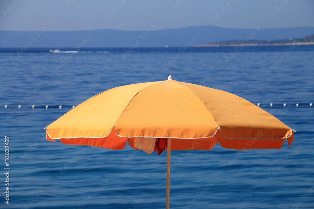 Orange beach umbrella near the Adriatic sea in Brela , Croatia
