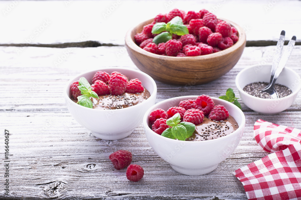 Chocolate banana smoothies with chia seeds served ripe raspberries and fresh mint on a light wooden background. The white ceramic bowls of serving healthy breakfast Chocolate banana smoothies with chia seeds served ripe raspberries and fresh mint on a light wooden background. The white ceramic bowls of serving healthy breakfast