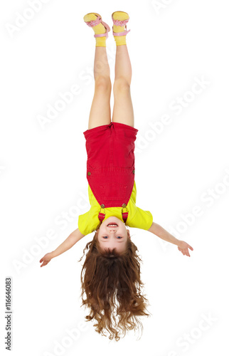 Cheerful little girl hangs upside down on white