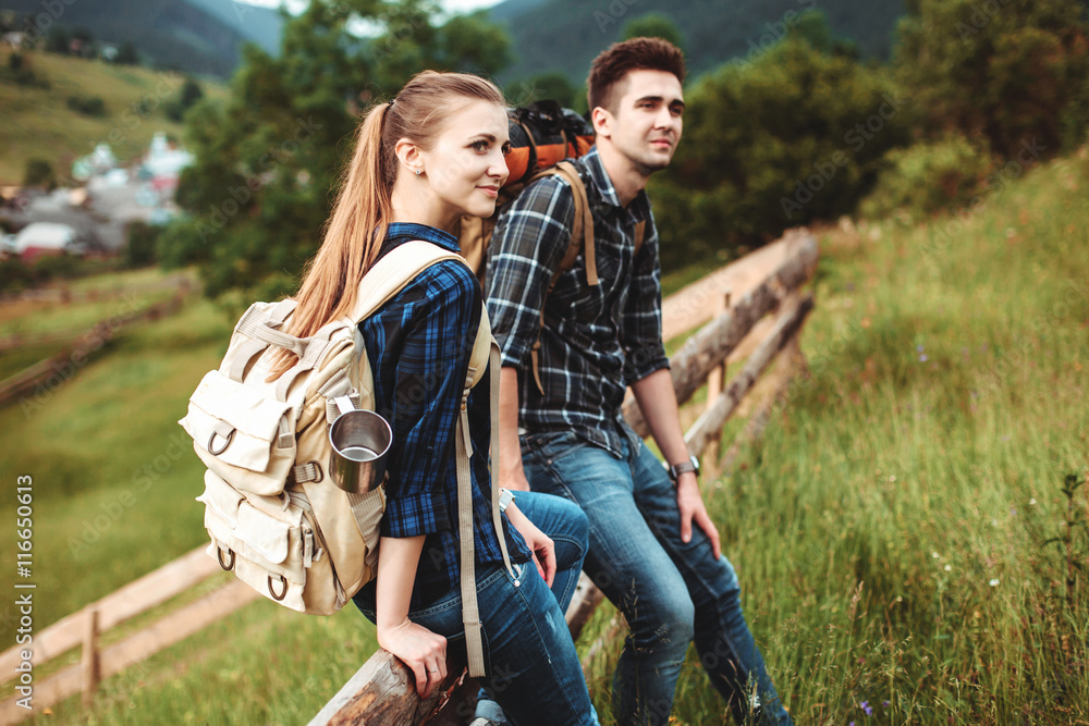 Fototapeta premium A couple of tourists sitting on a wooden fence and view beautiful countryside. The concept of active rest
