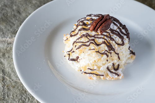 Coconut macaroon drizzled with chocolate on a white plate, highlighted by the sun
