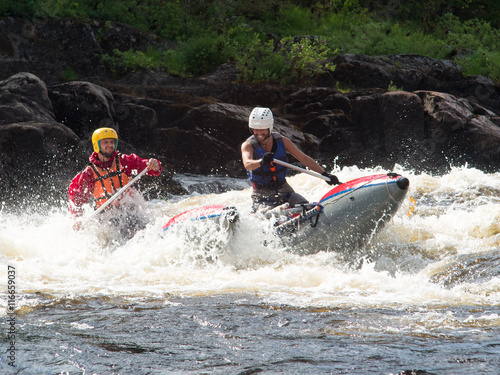 Two friends on an inflatable catamaran ride on the rough river with splashes