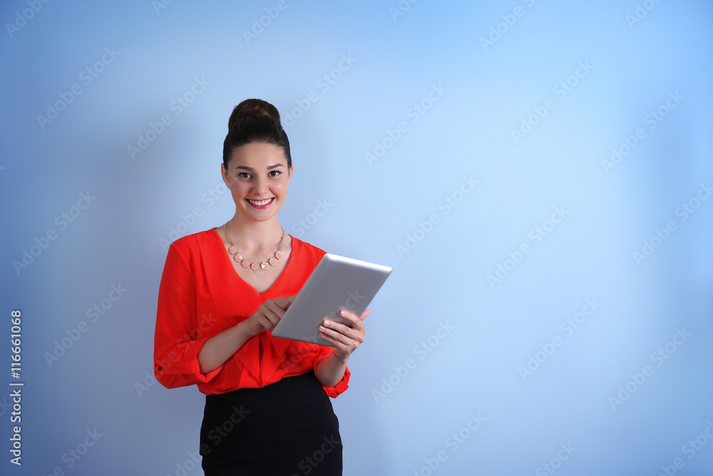 Pretty young woman holding tablet on light background