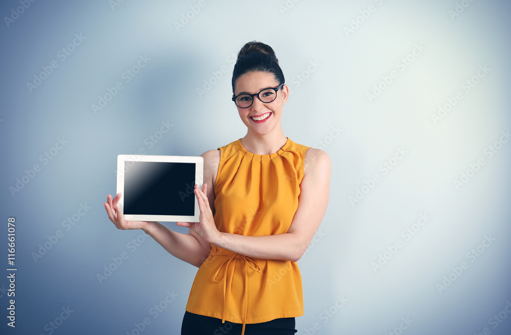 Beautiful young businesswoman holding tablet on light background