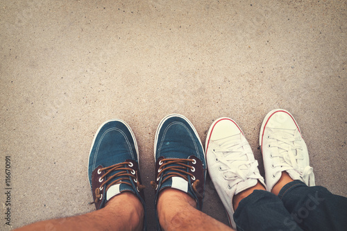 Love romantic couple - top view sneakers on the ground of man and woman feet in outdoor lifestyle. Fashion hipster retro trendy style. Travel and honeymoon trip in summer. vintage effect filter