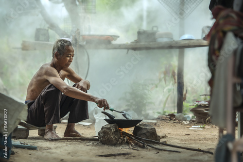 old man sitting and cooking outside his home,