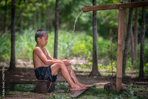 little boy bathing outdoor from a traditional bamboo chute,countryside Thailand.