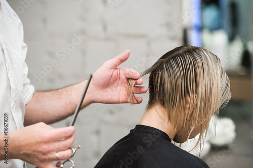 hairdresser cuts hair with scissors on crown of handsome satisfied client in professional hairdressing salon