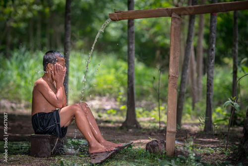 little boy bathing outdoor from a traditional bamboo chute,countryside Thailand.