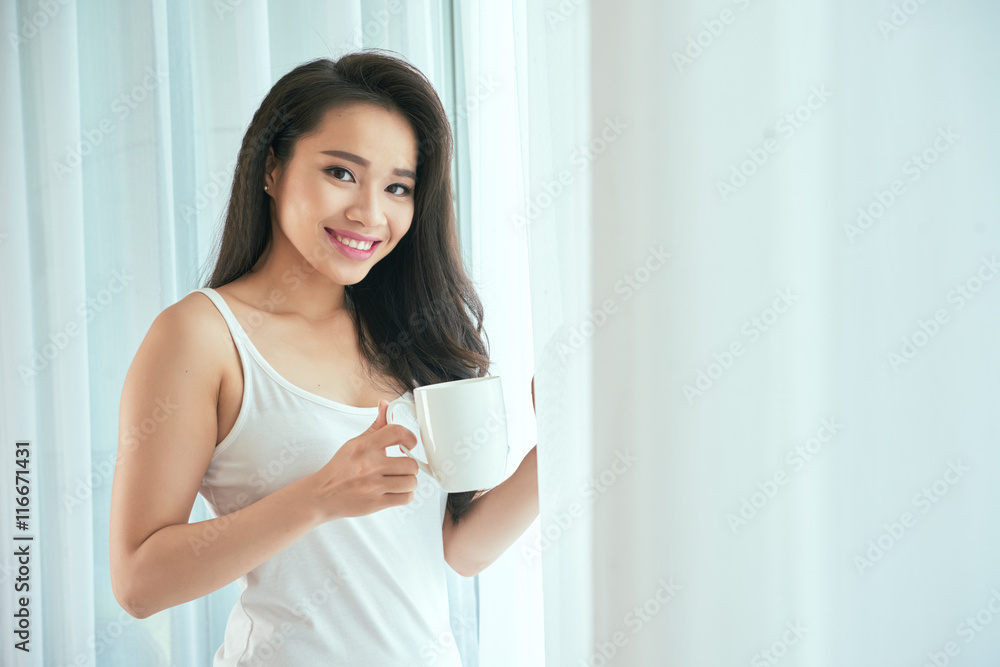 Vietnamese girl with coffee cup standing at window Vietnamese girl with coffee cup standing at window