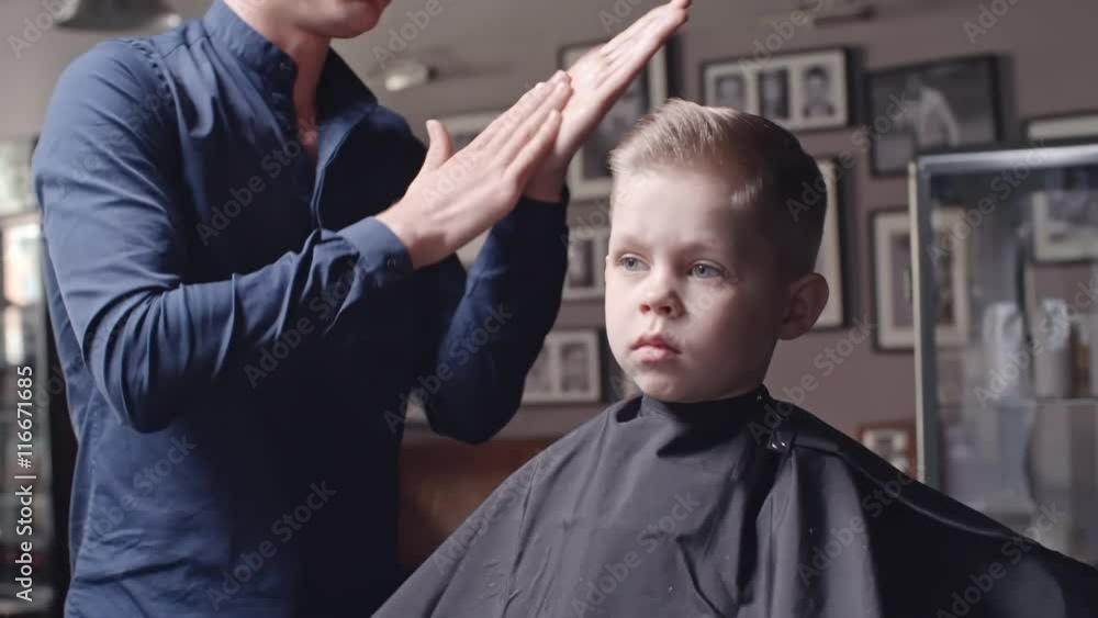 Hairstylist rubbing gel in his hands to fix new haircut of little boy Hairstylist rubbing gel in his hands to fix new haircut of little boy