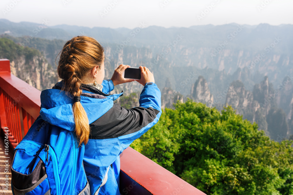 Female tourist with smartphone taking photo of mountains