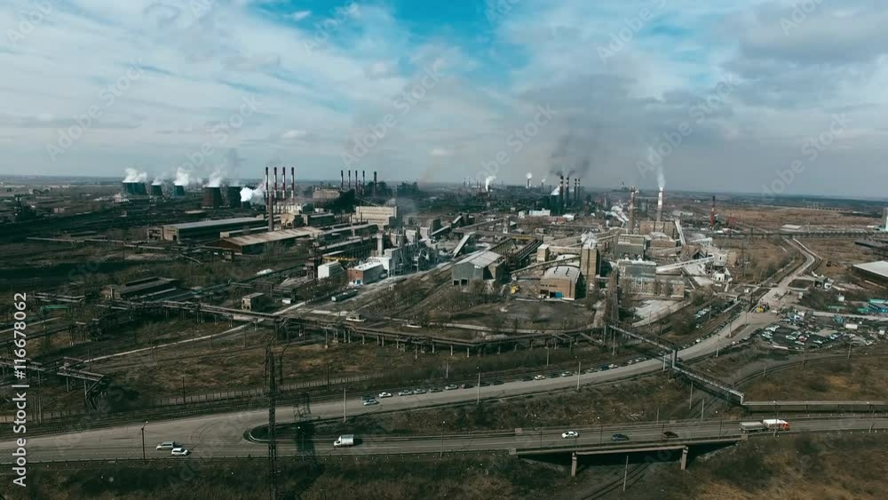 Aerial view of big metallurgical plant with chimneys smoking and polluting air, cars moving on roads nearby Aerial view of big metallurgical plant with chimneys smoking and polluting air, cars moving on roads nearby
