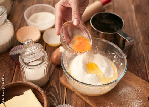 Woman hands, ingredients and devices for preparation muffin on a wooden background. House pastries. Food concept. Flour, eggs, butter, mix for pastries. 