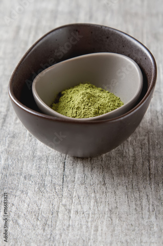 Dry Matcha tea in a small brown plate. Grey wood background