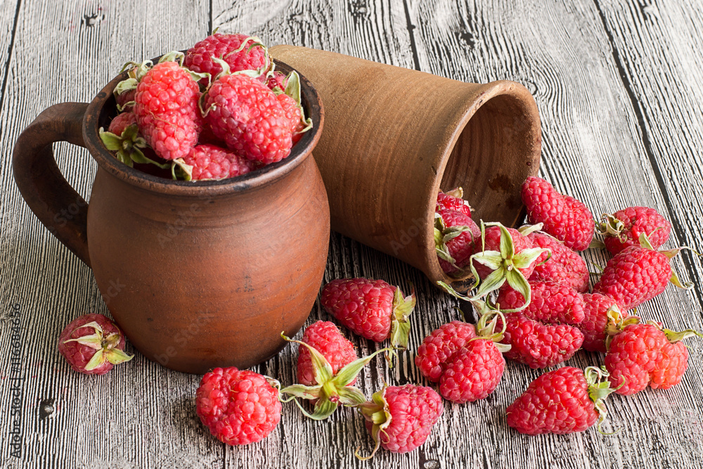 Raspberries. Raspberries in a clay mug and in a glass on a gray wooden table. Raspberries. Raspberries in a clay mug and in a glass on a gray wooden table.