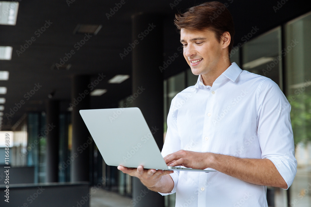Cheerful businessman standing and using laptop Cheerful businessman standing and using laptop