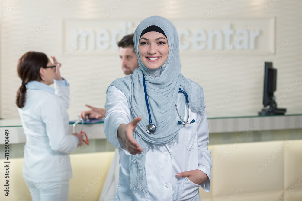 Obraz premium Young happy smiling female muslim doctor giving hand for handshaking.