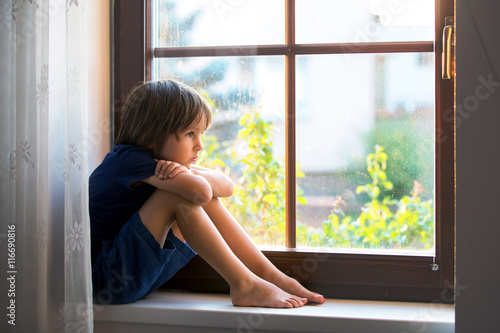 Sad child, boy, sitting on a window shield photo