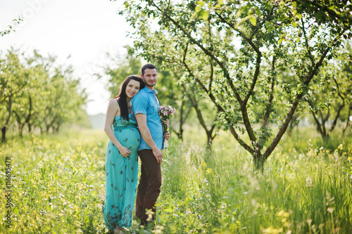 Happy pregnant couple at turquoise dress on the garden