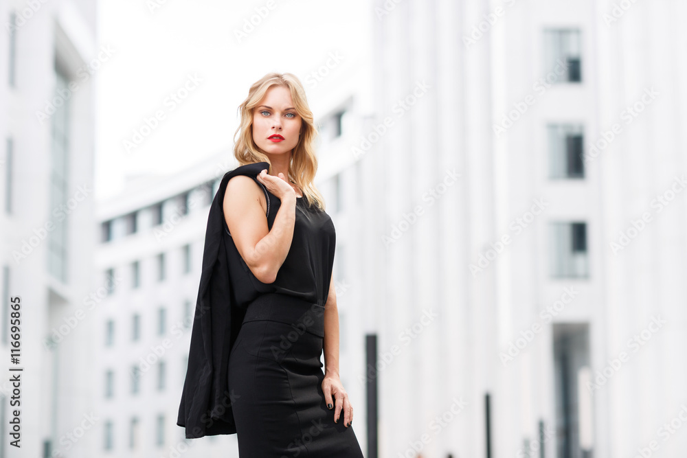 Serious successful businesswoman in black suit against white office building Serious successful businesswoman in black suit against white office building