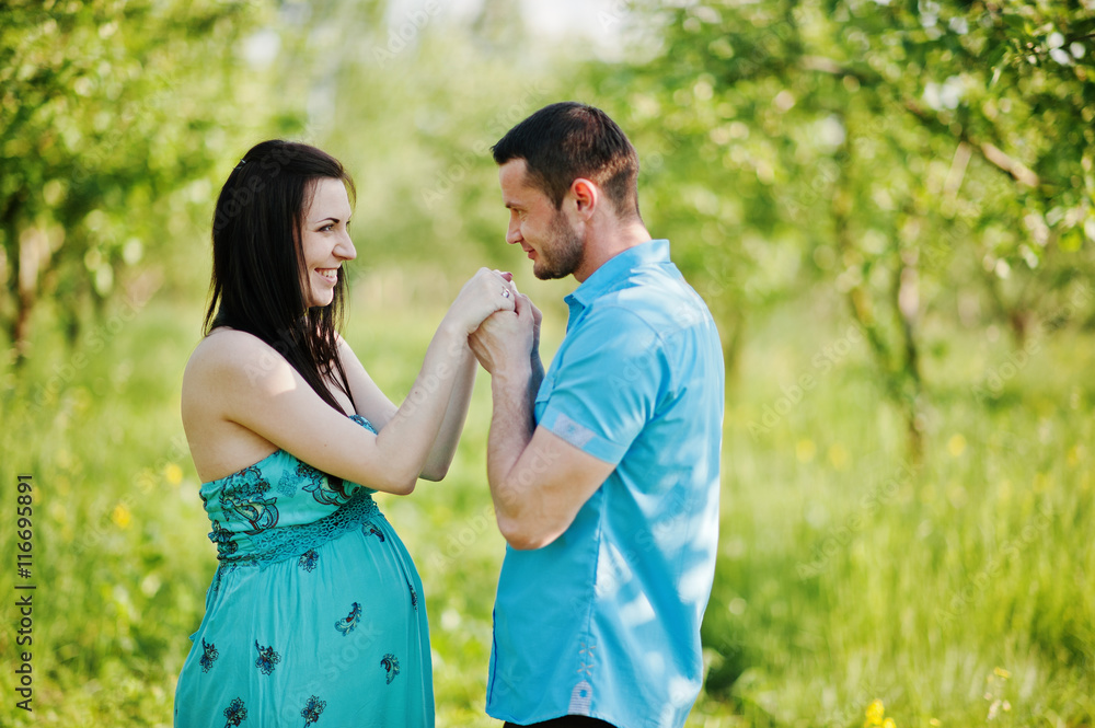 Happy pregnant couple at turquoise dress on the garden