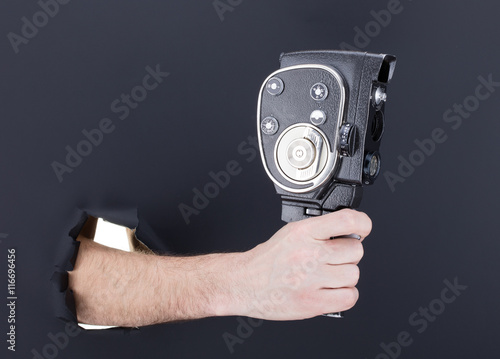 Male hand breaking through the black paper background and holding retro camera