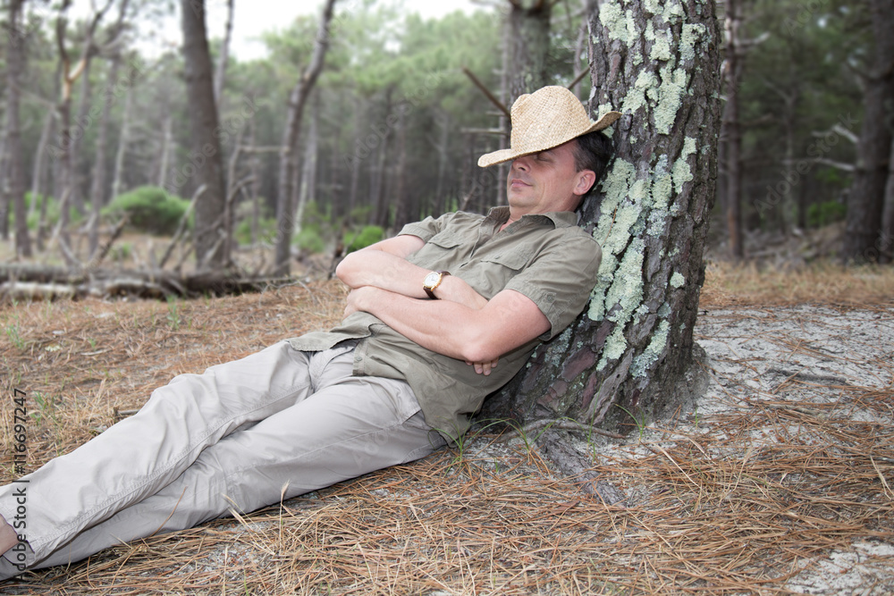 Cheerful and quiet man relaxing leaning on Tree with hat