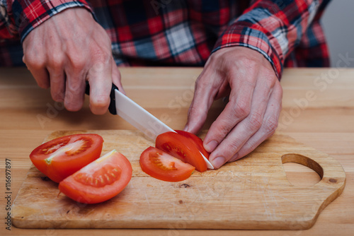 Man hands slicing fresh tomato by ceramic knife