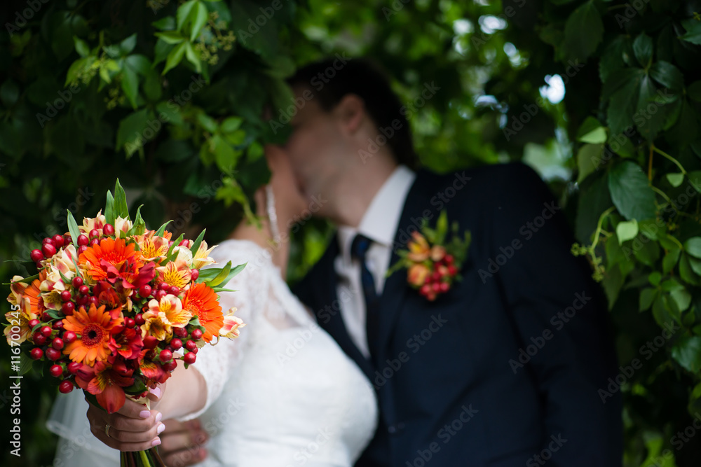 Fototapeta premium blur background with wedding bouquet and newlyweds kiss, shallow
