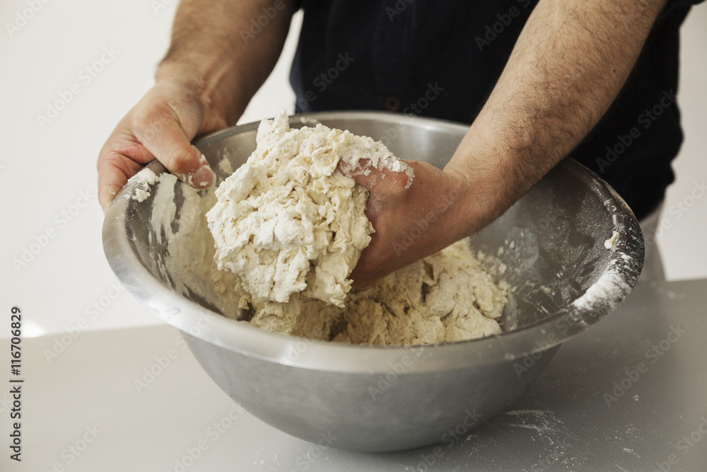 Close up of a baker kneading bread dough in a metal mixing bowl. Close up of a baker kneading bread dough in a metal mixing bowl.