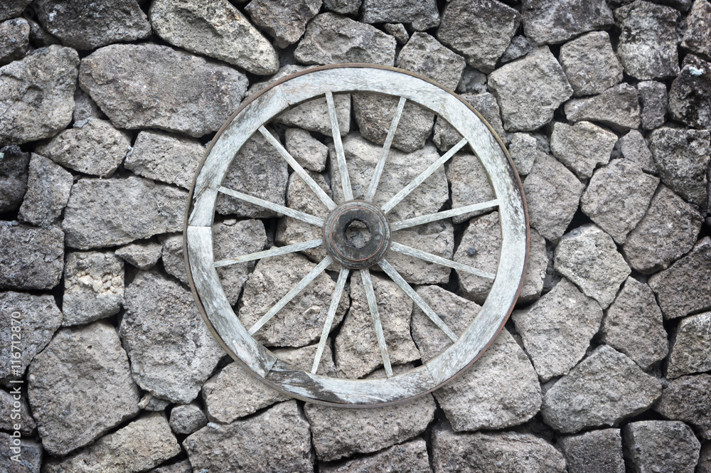 Wooden wagon wheel on a stone back ground.