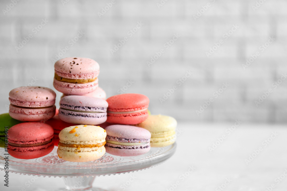 Fototapeta premium Colorful tasty macaroons in glass stand on blurred brick wall background