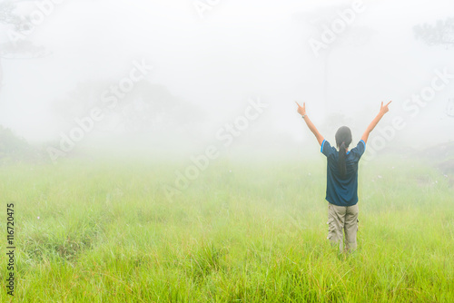 Happy young woman rising hand and enjoying misty day on green morning