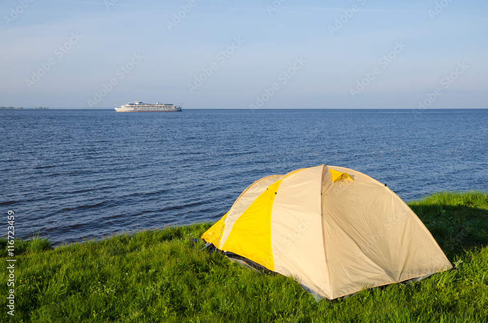 The River Kama. Tourist tent on the shore of the Kuibyshev reservoir. On the horizon floats a tourist motor ship.