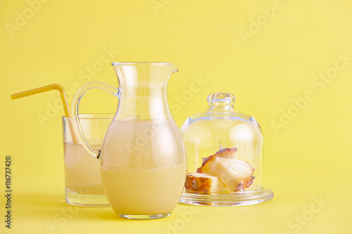 Glass jug of fresh pineapple juice on yellow