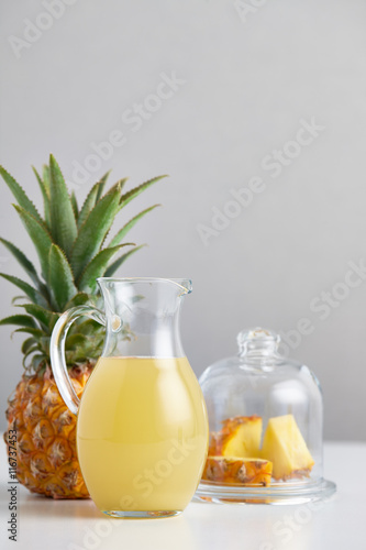 Glass jug with pineapple juice and fruit on table